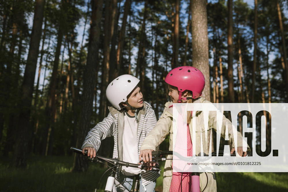 IMAGO Creative: Klimawandel - Umwelterziehung Girl and boy talking while riding bicycles in forest model released Symbolfoto EYAF01084