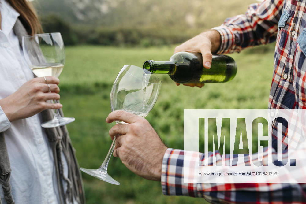 IMAGO Creative, Sommer, Weinfeste und Weinwanderungen Man serving white wine in glass while standing with woman at vineyard model released Symbolfoto JRFF04491
