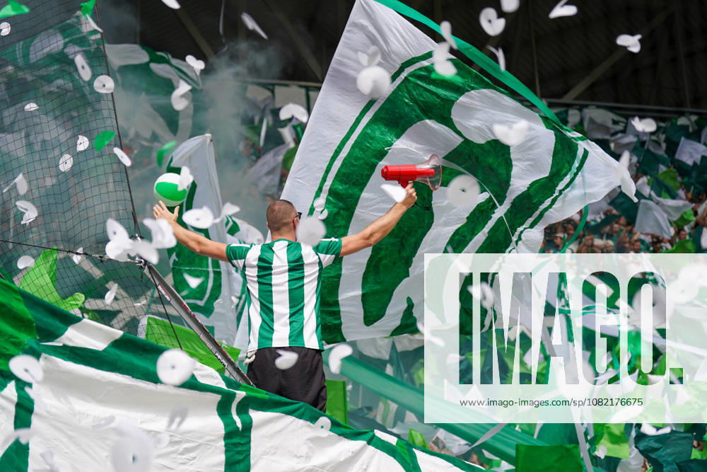 Deutschland: Fussball Bundesliga Saison 2026 - 2027, 1. Spieltag - SC Freiburg vs Werder Bremen - Europa Park Stadion (Freiburg): Fankurve von Werder Bremen im Stadion: Vorsänger mit Megafon vor dicht gedrängten Fans, umgeben von großen grün-weißen Schwenkfahnen. Grüner Rauch, Konfetti und Luftschlangen prägen die Choreographie. Zuschauer, Fans, Ultras, Supporter, Tribüne, Fanblock, Fankultur, Fanchoreo, Choreographie, Fahnenmeer, Megafon, Rauch, Pyrotechnik, Konfetti, Stimmung, Emotionen.
