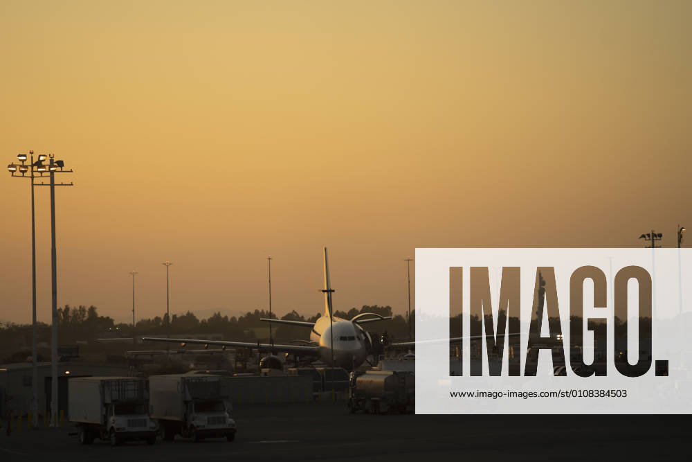 Distant shiny aircraft surrounded with service vehicles on airfield in sunset in USA, Model released