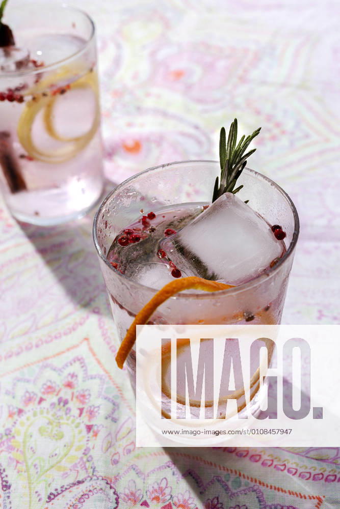 Gin tonic cocktail with pink tonic water, pink pepper, rosemary, mint,cinnamon,lemon and orange in the sunlight on a restaurant table
