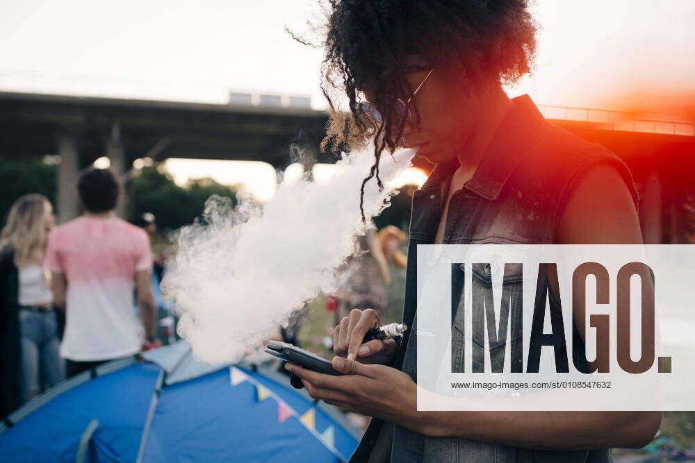 Side view of young man smoking while using mobile phone at music event , model released
