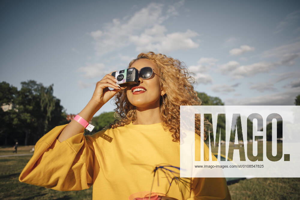 Smiling young woman photographing with camera on field against sky , model released