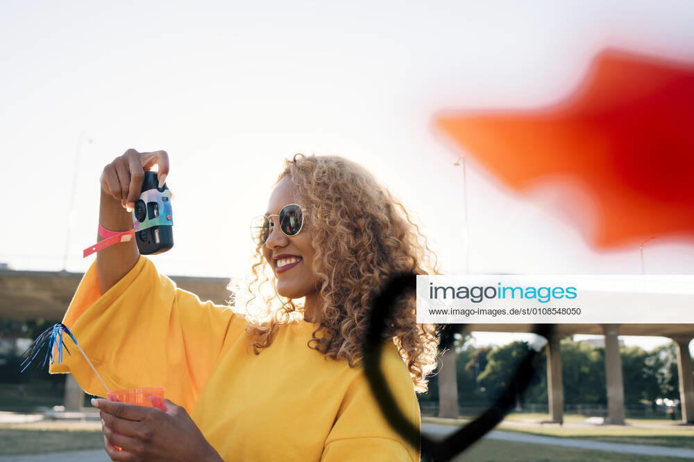 Smiling young woman photographing with camera against sky at event on sunny day , model released