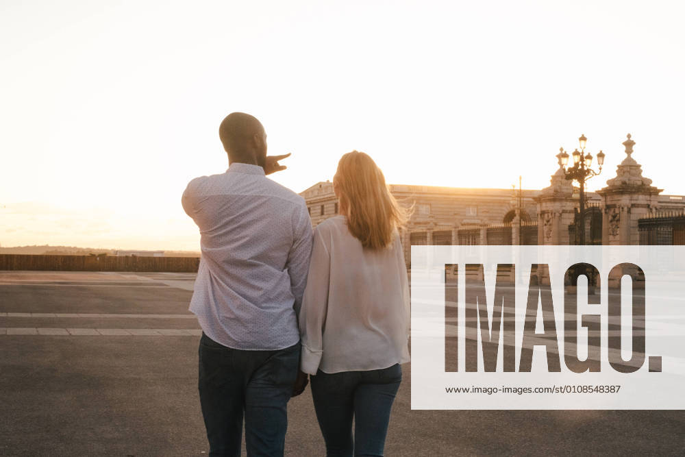 IMAGO Creative: Sommer, Abendspaziergang Back view anonymous diverse couple in casual outfits walking together along asphalt sidewalk on street during sunset time, Model released