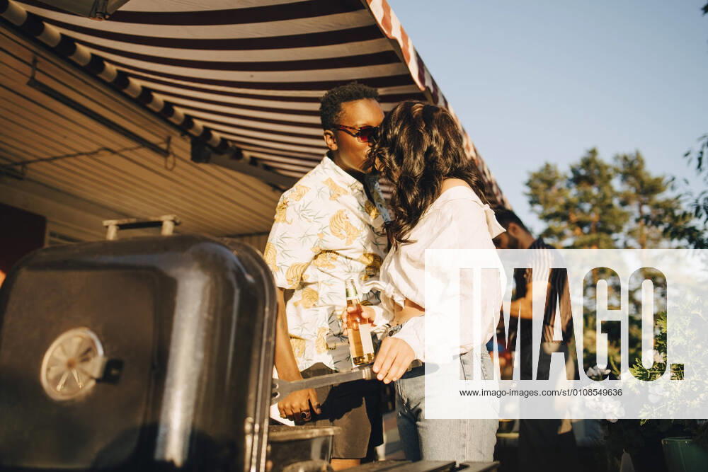 Girlfriend kissing boyfriend while standing by barbecue grill in party , model released, property released