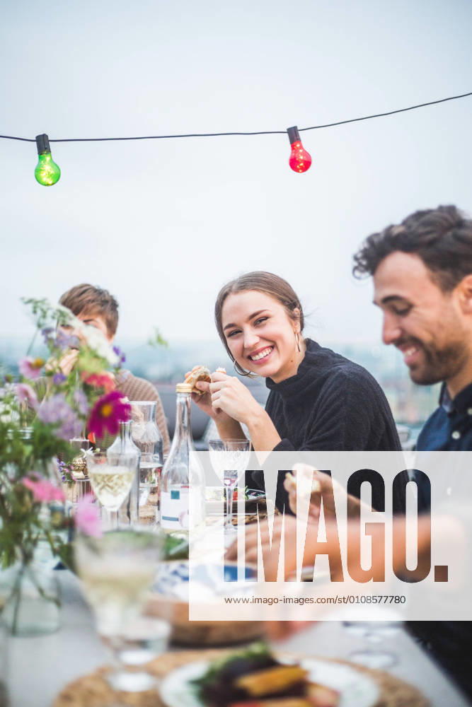 IMAGO Kreativ: Urbane Kultur - Sommer auf den Dächern Portrait of smiling female sitting with friends during social gathering on terrace , model released, property released