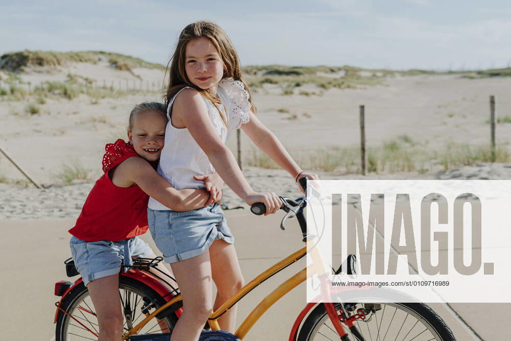 IMAGO Creative: Schwesternschaft Younger sister embracing girl while sitting on bicycle during sunny day model released Symbolfoto OGF00609