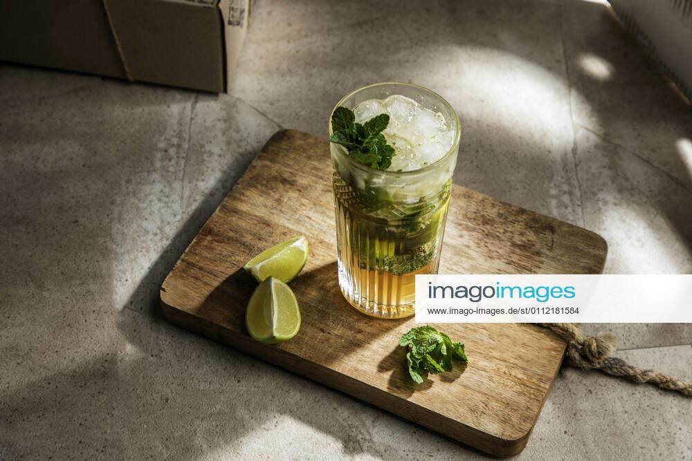 From above of refreshing cold alcoholic mojito with ice mint leaves and cut lime on wooden board