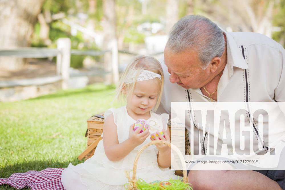 Lovely grandfather and granddaughter enjoy easter eggs on a picnic blanket in the park