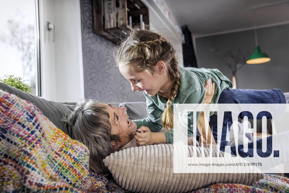 IMAGO Creative: Hygge - Winter Innendesign Grandmother playing with granddaughter while lying on sofa at home model released Symbolfoto property released AUF00617
