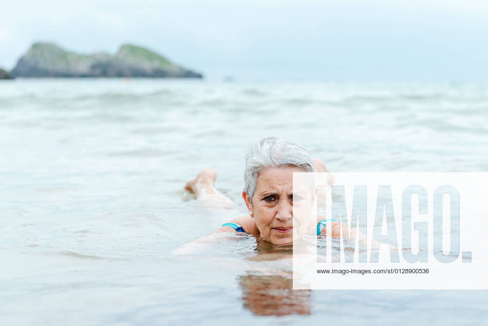 IMAGO Creative: Sommer Sport - Strand Active senior gray haired female swimming in ocean water while enjoying summertime and practicing healthy lifestyle on seashore, Model released AlbertoMenendez_OldWomanBeach_25.jpg