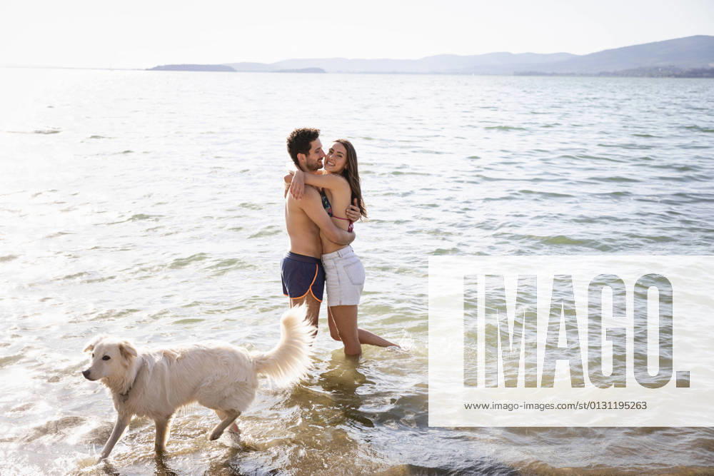 Smiling couple embracing while standing by dog in lake model released Symbolfoto property released EIF01720