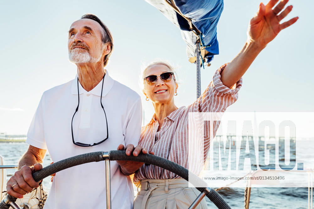 Mature couple standing at steering wheel on their yacht and enjoying vacation Mature couple standing at steering wheel on their yacht and enjoying vacation