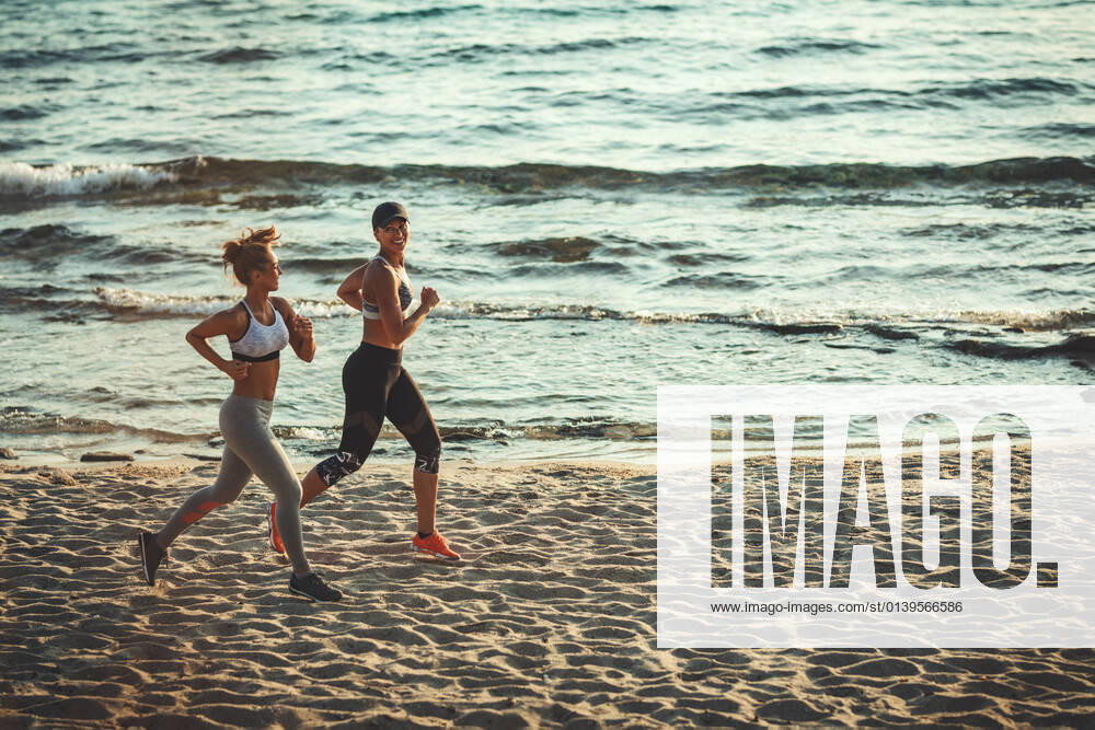 IMAGO Creative: Sommer Sport - Strand Freedom Two smiling happy young women are running along the sea shore on the beach during the hot summer vacation day.