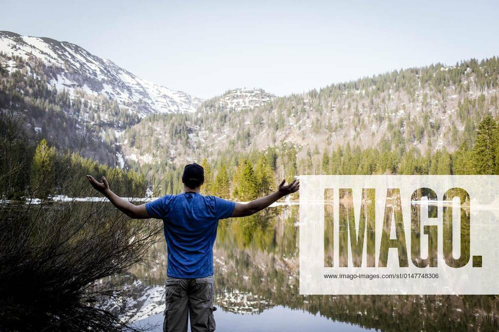IMAGO Creative: Sommer, In den Bergen young man with cap and blue shirt is standing in front of mountain lake model released, Symbolfoto, 12.10.2020,