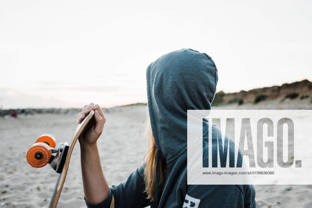 IMAGO Creative: Sommer Sport - Strand woman with her hood up at the beach holding skateboard at sunset Christchurch, England, United Kingdom CR_RABE210920-830236-01 ,model released, Symbolfoto