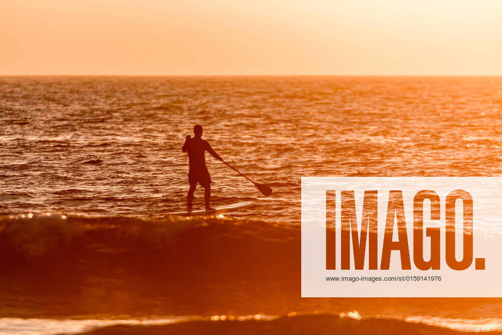 IMAGO Creative: Sommer Sport - Strand Stand up paddler silhouette at sunset. Concept about sport, surf, vacations and people., model released, , 22483792.jpg, Sport, athlete, beach, board, boarding, challenge, cool, europe, fun, green, lifestyle, male, man, nature, ocean, orange, outdoor, paddle, people, person, portugal, row, sea, sports, spray, stand, summer, sunset, surf, surfer, surfing, travel, tropical, up, water, wave, young,