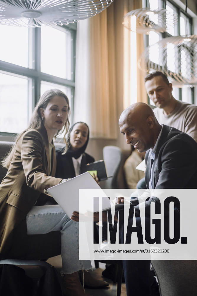 IMAGO Creative: Business, Innovative Technologie-Lösungen Mid adult businesswoman discussing over laptop with bald businessman by colleagues in creative office Sweden, Stockholm, model released, property released