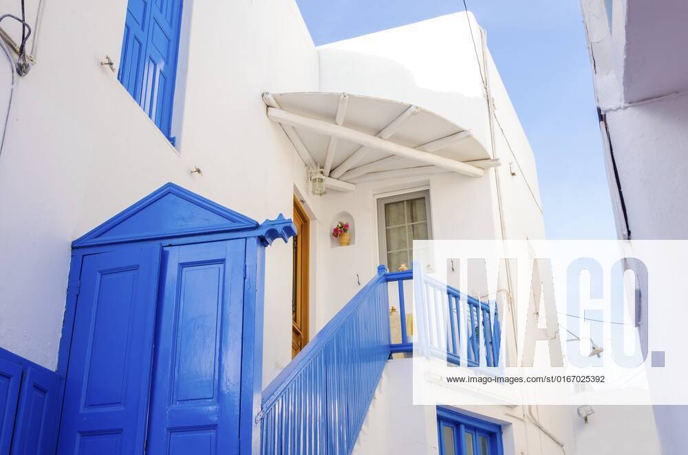 A very traditional alley view of the architecture in Chora, on the greek island Mykonos, Greece. A blue door, fence and windows of a whitewashed house against the blue sky. , 21668310.jpg, mykonos, greece, architecture, greek island, travel, greek, blue, alley, mikonos, myconos, chora, island, destination, summer, whitewashed, fence, picturesque, door, alleyway, traditional, tourist, frame, colourful, street, town, hora, stone, houses, winds, white, typical, landmark, attraction, holiday, sunny, aegean, sun, village, building, window, sightseeing, cosmopolitan, city, cyclades, tourism, mediterranean, vacation, capital, santorini, hellas,