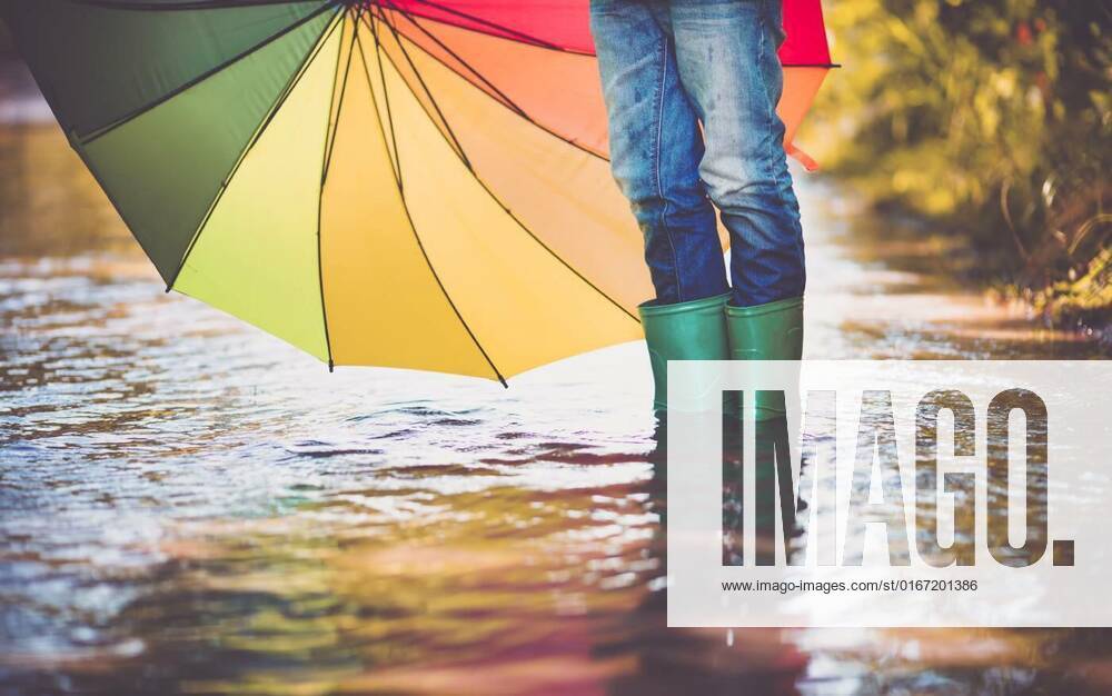Child walking in wellies in puddle on rainy weather, Child walking in wellies in puddle on rainy weather. Boy holding colourful umbrella under rain in summer, Child walking in wellies in puddle on rainy weather. Boy holding colourful umbrella under rain in summer model released, Symbolfoto , 03.08.2021,