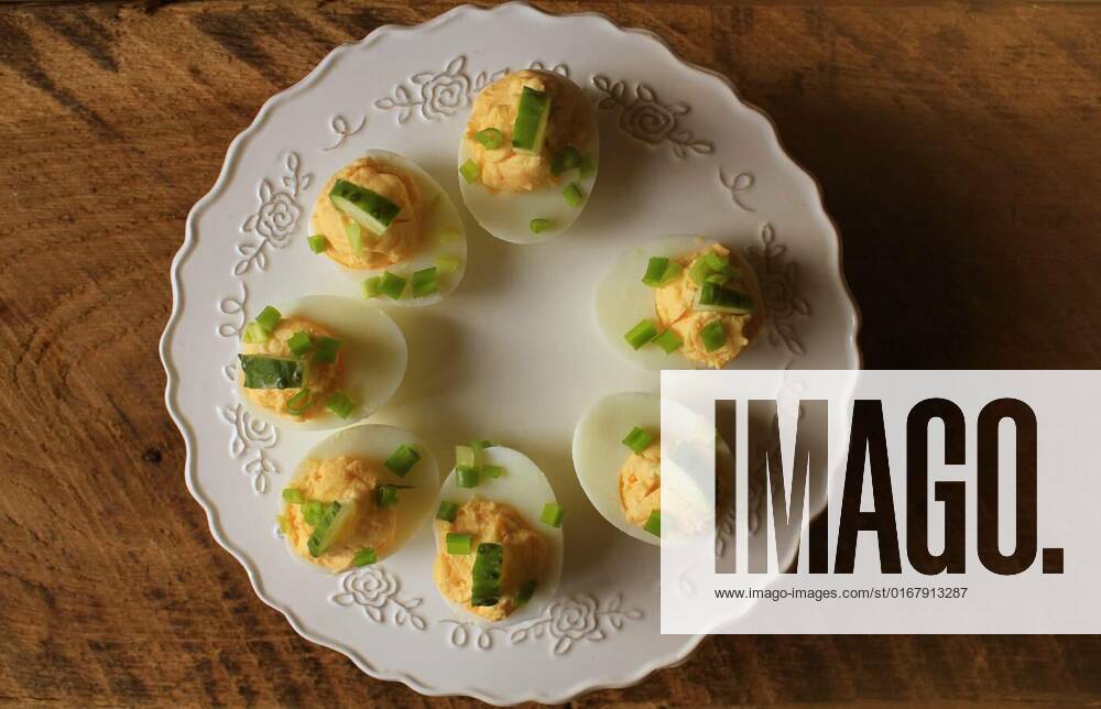 Spicy deviled eggs garnished with cucumber and leek on white plate. Top view. Wooden rustic background, Spicy deviled eggs garnished with cucumber and leek on white plate. Top view. Wooden rustic background ., Spicy deviled eggs garnished with cucumber and leek on white plate. Top view. Wooden rustic background ., 07.02.2022,