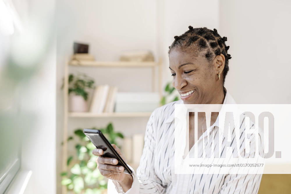 IMAGO Creative: Business, Innovative Technologie-Lösungen Smiling woman using smart phone at home model released, Symbolfoto property released, JCZF01075