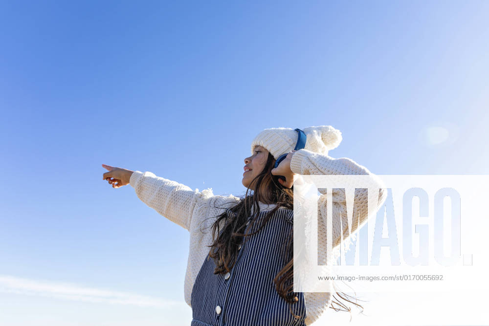 IMAGO Creative: Business, Innovative Technologie-Lösungen Girl enjoying music through headphones gesturing in front of blue sky model released, Symbolfoto, MEGF00101