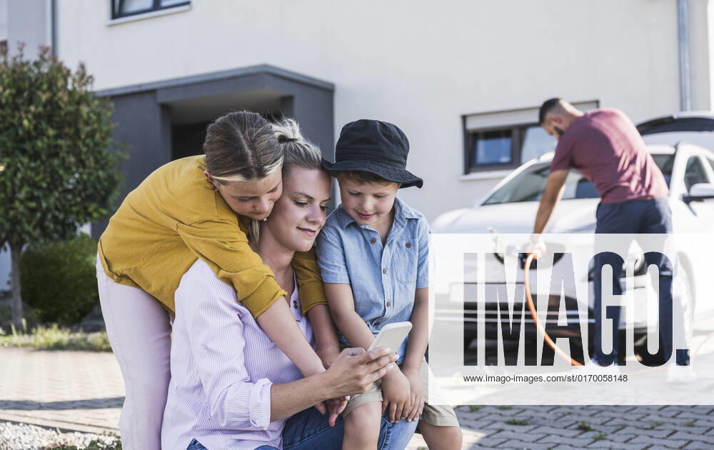 IMAGO Creative: Business, Innovative Technologie-Lösungen Mother and children checking smartphone while father is charging electric car model released, Symbolfoto property released, UUF27090