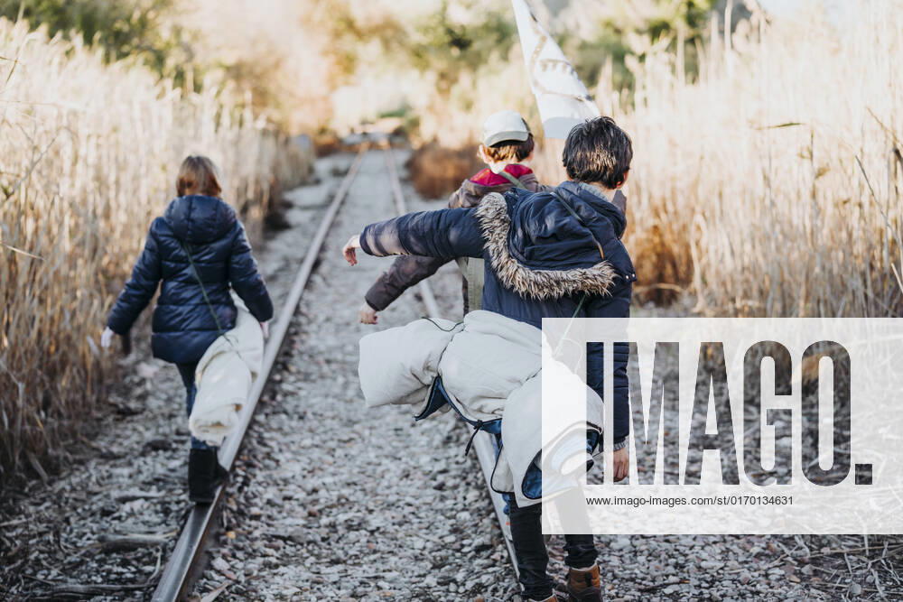 Back view of unrecognizable group of three children hiking in the woods walking in a train track, Model released JoseLuisCarrascosa_AdventureBoys_4