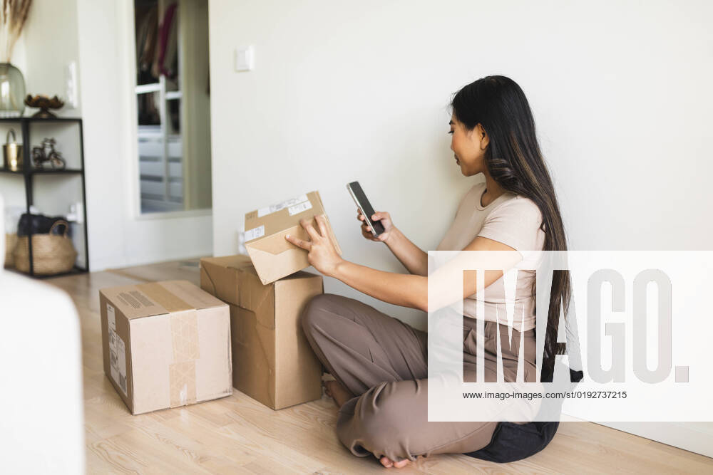 IMAGO Creative: Business, Innovative Technologie-Lösungen Young woman checking and taking picture of delivery package box through smart phone at home model released, Symbolfoto property released, DMMF00232