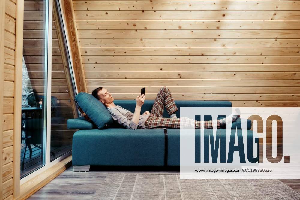Middle-aged man on couch browsing internet, surfing web, using online app, Middle-aged man on couch in his bungalow browsing internet, surfing web, using online app, Middle-aged man on couch in his bungalow browsing internet, surfing web, using online app model released, Symbolfoto , 06.11.2022,