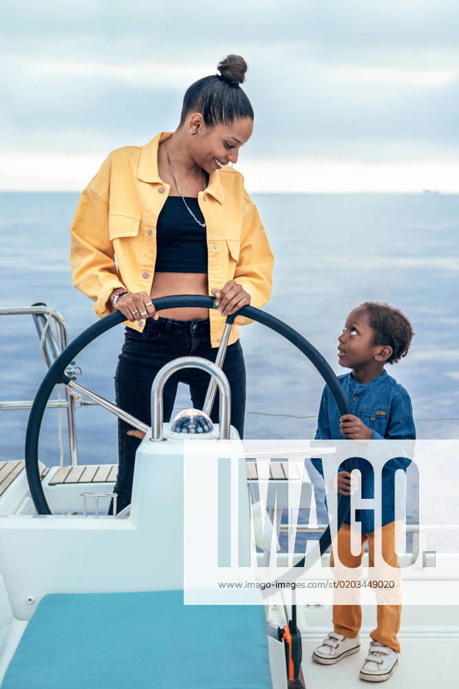 Cheerful African American mother and son standing together at steering wheel while looking at each other during weekend on yacht, Model released AlfonsoSaenz_ID12778_387464_047