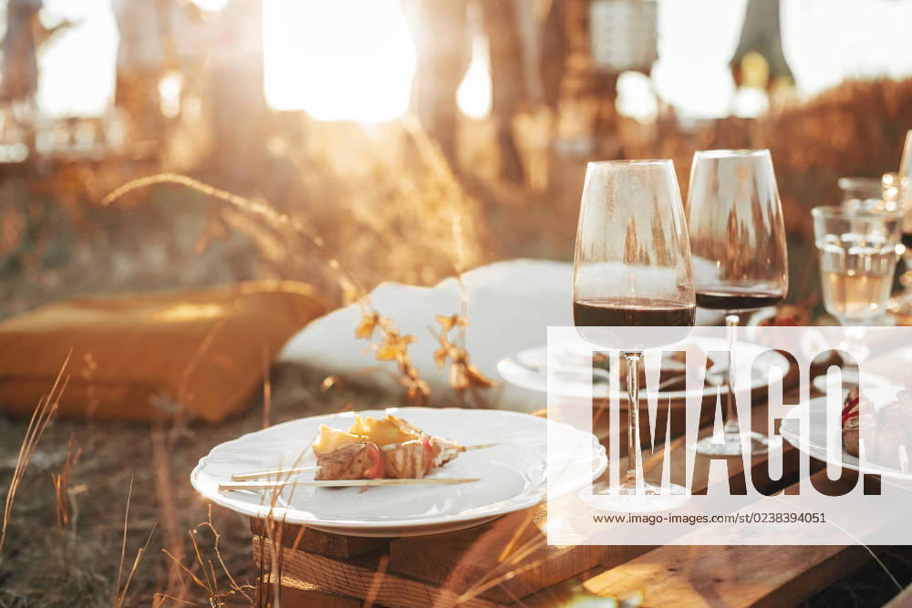Wooden table with glassware arranged for picnic Set of elegant glassware placed on plank wooden table with floral arrangement on grassy meadow during festive autumn picnic