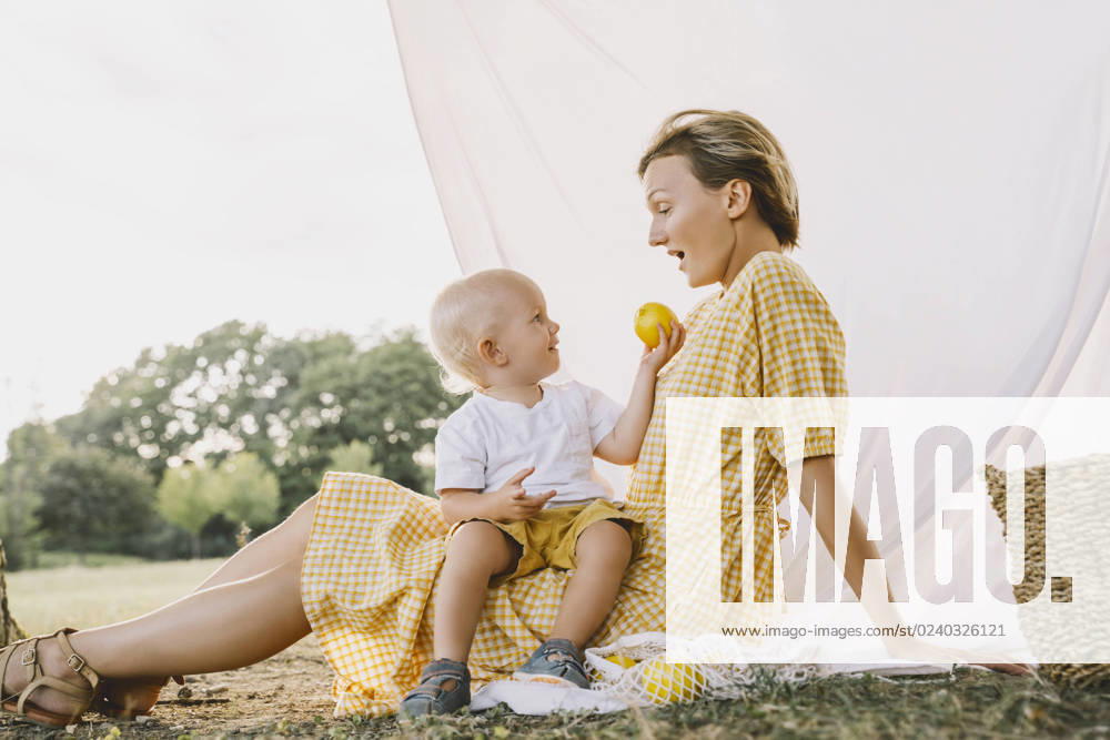 Smiling boy giving fruit to mother sitting in park model released, Symbolfoto, NDEF00399