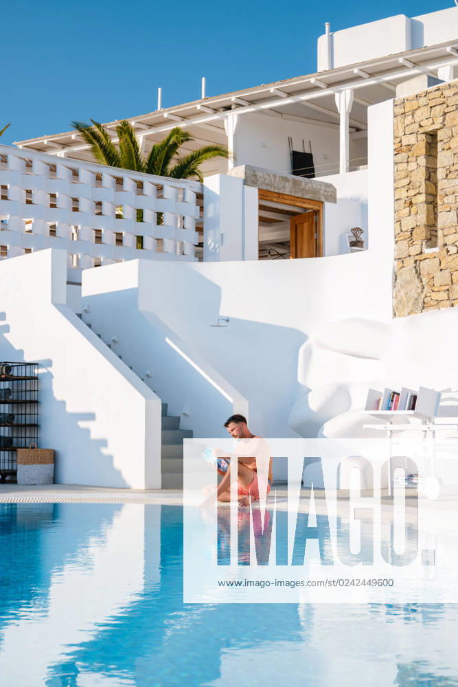 Young men reading a book by the swimming pool during vacation Young men read a book by the swimming pool during vacation. a young man in a swim shorts by the pool during vacation ,model released, Symbolfoto