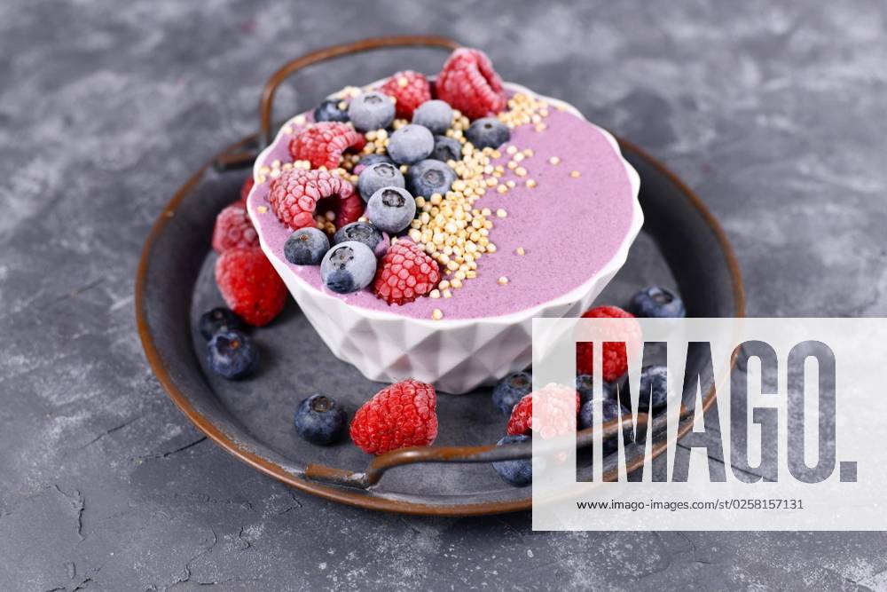 Fruit smoothie bowl with pink yogurt decorated with healthy raspberry, blueberry and puffed quinoa grain on iron tray
