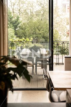 Wooden table and flower in light room near transparent door of terrace with wooden table and green plant near fence and trees in city {{table,terrace,room,style,interior,design,plant,decor,flower,veranda,apartment,door,transparent,potted,entrance,leaf,dwell,decoration,fence,wooden,light,home,summer,tree,domestic,chair,seat,creative,flat,residential,flowerpot,green,modern,estate,material,glass,property,floral,clean,part,fencing,barrier,vertical,inside}}