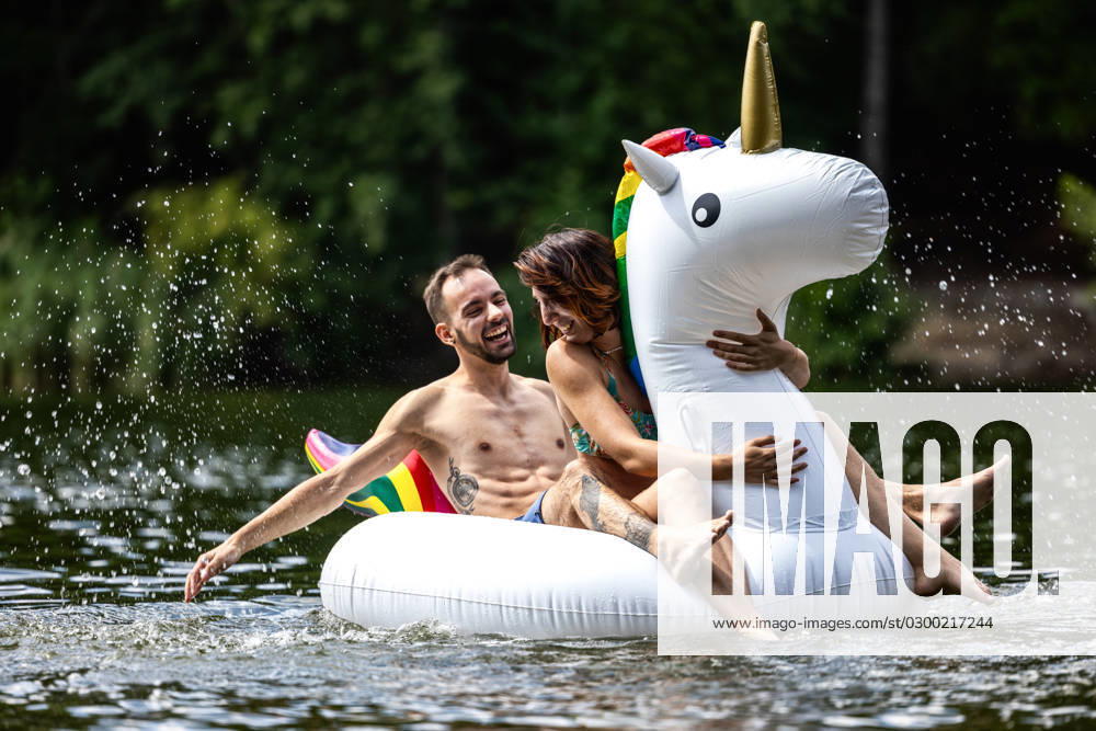CREATIVE - Paar am See in Berlin Berlin, Deutschland - 25. Juli 2023: (CREATIVE) Ein Mann und eine Frau (Models) genießen auf einem aufgeblasenen Einhorn einen Sommertag an der Krummen Lanke, einem See in Berlin. Berlin