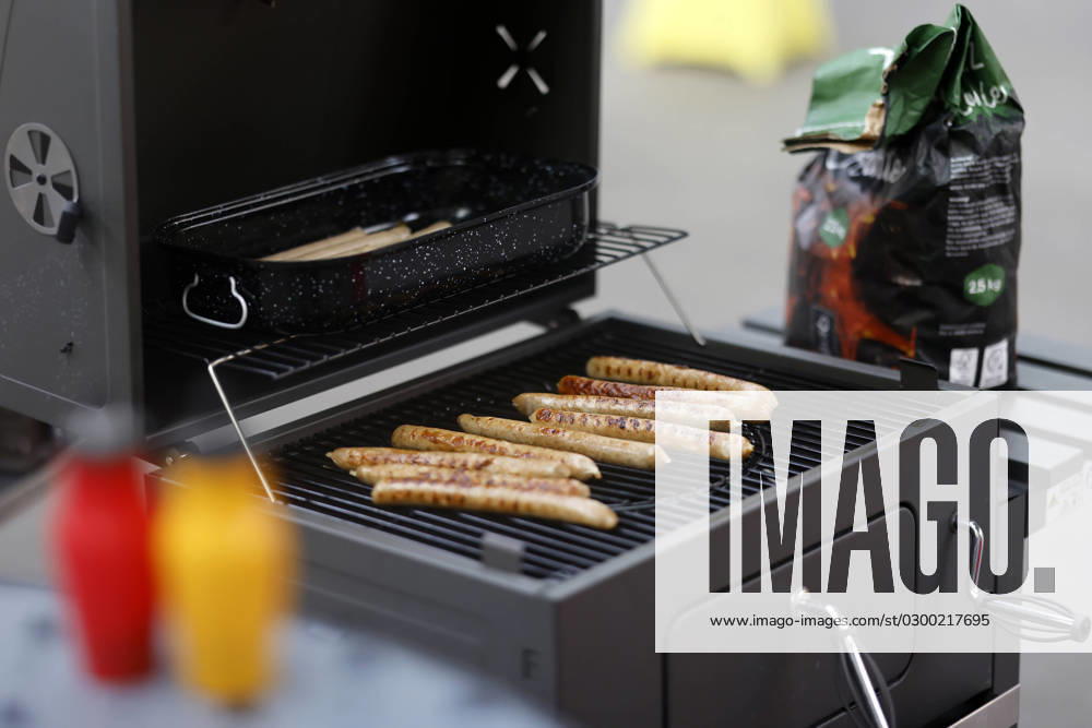 Grilled sausages lie on a coal grill In the foreground ketchup and mustard Theme image, symbol image Cologne, 25 07 2023 NRW Germany