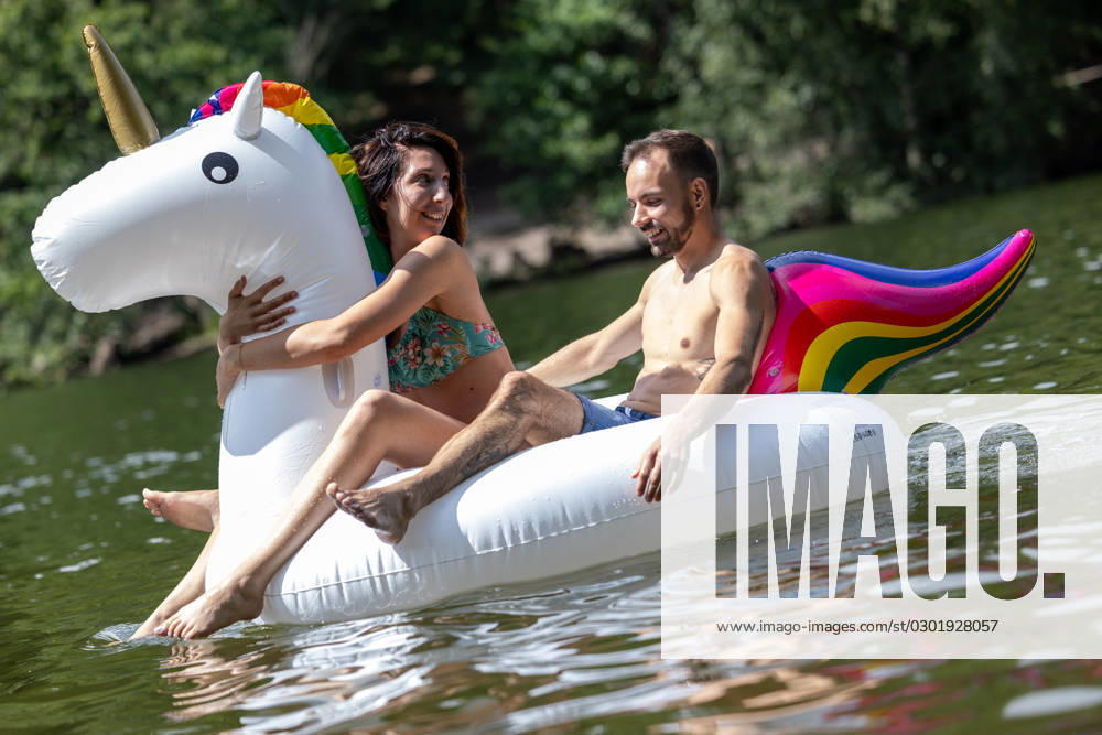CREATIVE - Paar am See in Berlin Berlin, Deutschland - 25. Juli 2023: (CREATIVE) Ein Mann und eine Frau (Models) genießen auf einem aufgeblasenen Einhorn einen Sommertag an der Krummen Lanke, einem See in Berlin. Berlin
