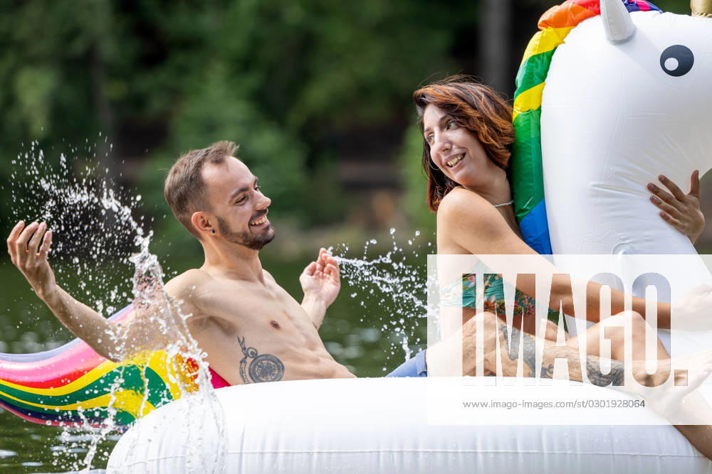 CREATIVE - Paar am See in Berlin Berlin, Deutschland - 25. Juli 2023: (CREATIVE) Ein Mann und eine Frau (Models) genießen auf einem aufgeblasenen Einhorn einen Sommertag an der Krummen Lanke, einem See in Berlin. Berlin