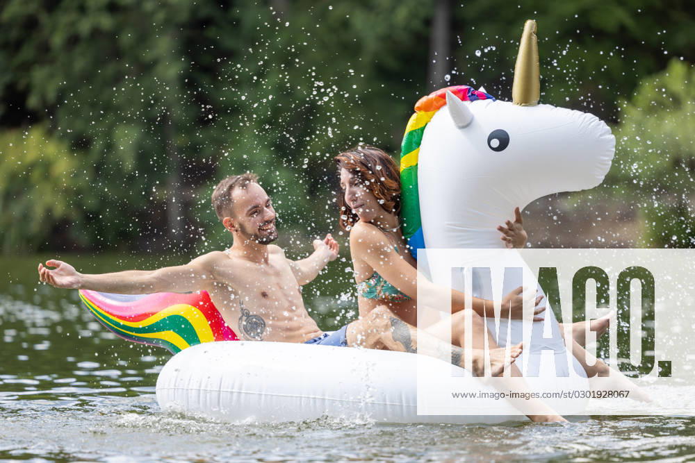 CREATIVE - Paar am See in Berlin Berlin, Deutschland - 25. Juli 2023: (CREATIVE) Ein Mann und eine Frau (Models) genießen auf einem aufgeblasenen Einhorn einen Sommertag an der Krummen Lanke, einem See in Berlin. Berlin