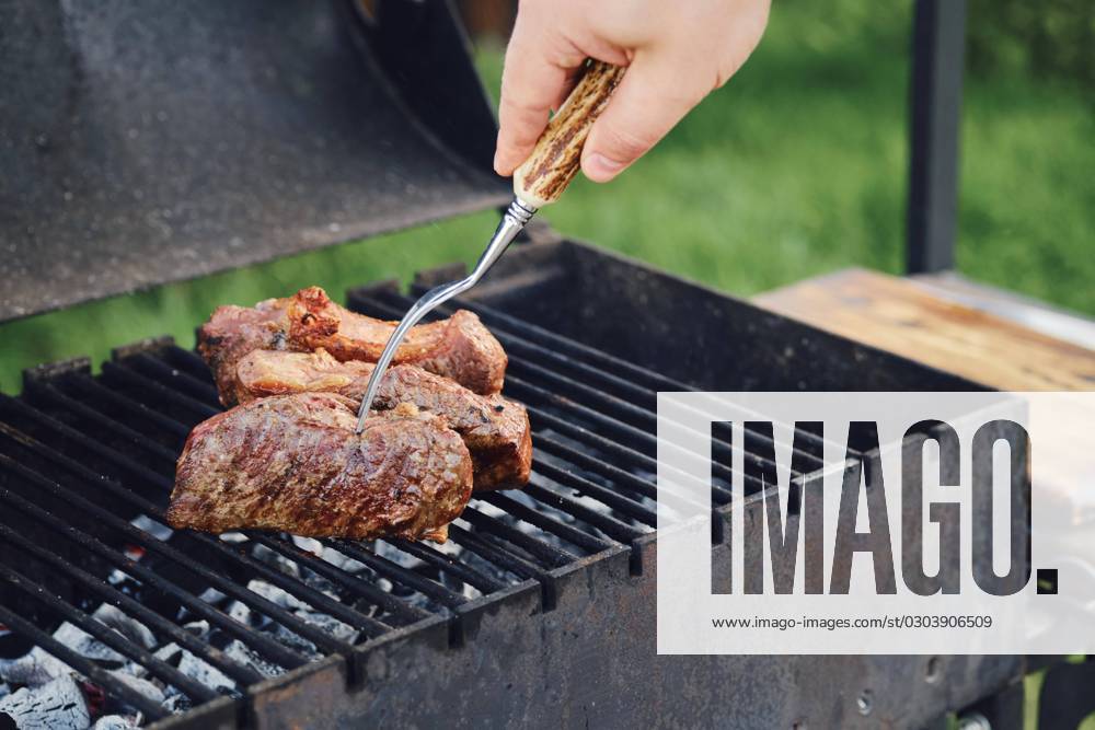 Unknown Man at Barbecue one Steaks at Free he turns the Meat with a Fork