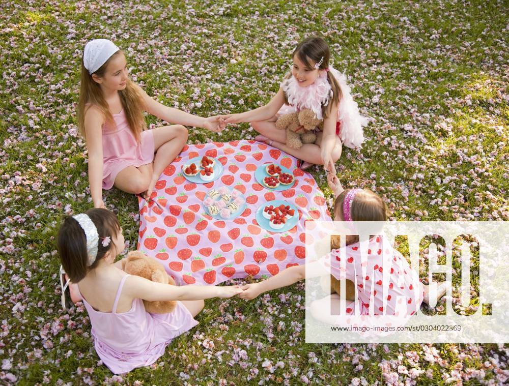 Four young girl sitting around a colorful blanket holding hands and having a party United Kingdom