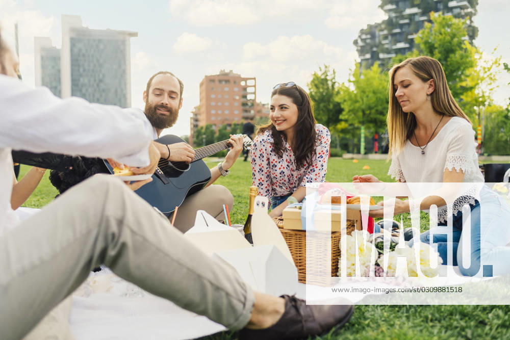 Smiling man playing guitar with friends enjoying picnic in park model released, Symbolfoto, MEUF09214