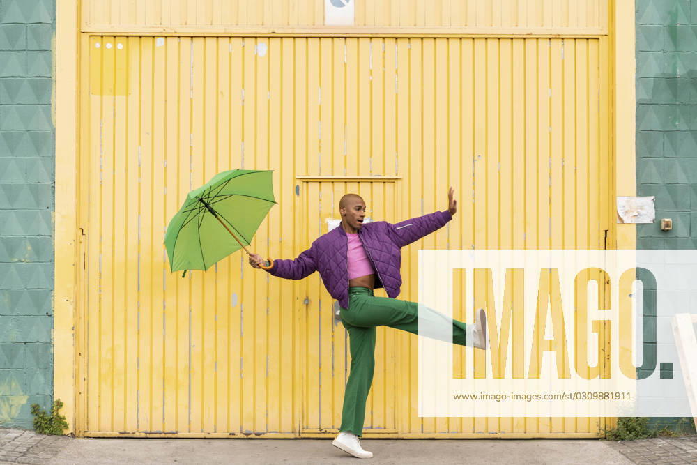 Non-binary person dancing with green umbrella in front of yellow shutter door model released, Symbolfoto, AFVF09352