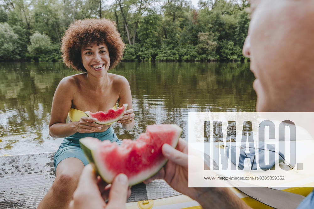Smiling woman eating watermelon with friend on paddleboard in lake model released, Symbolfoto, YTF01035
