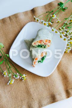 A vertical High angle closeup of a salmon wrap sliced in half appetizing, closeup, cooked, cuisine, cut, diet, dining, dinner, dish, eating, fish, food, fresh, half, healthy, high angle, lunch, meal, nutrition, plate, protein, recipe, salmon, sandwich, seafood, sliced, tasty, vertical, wrap