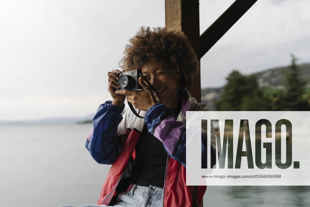 Smiling young woman photographing with camera near lake model released, Symbolfoto, BOYF02034